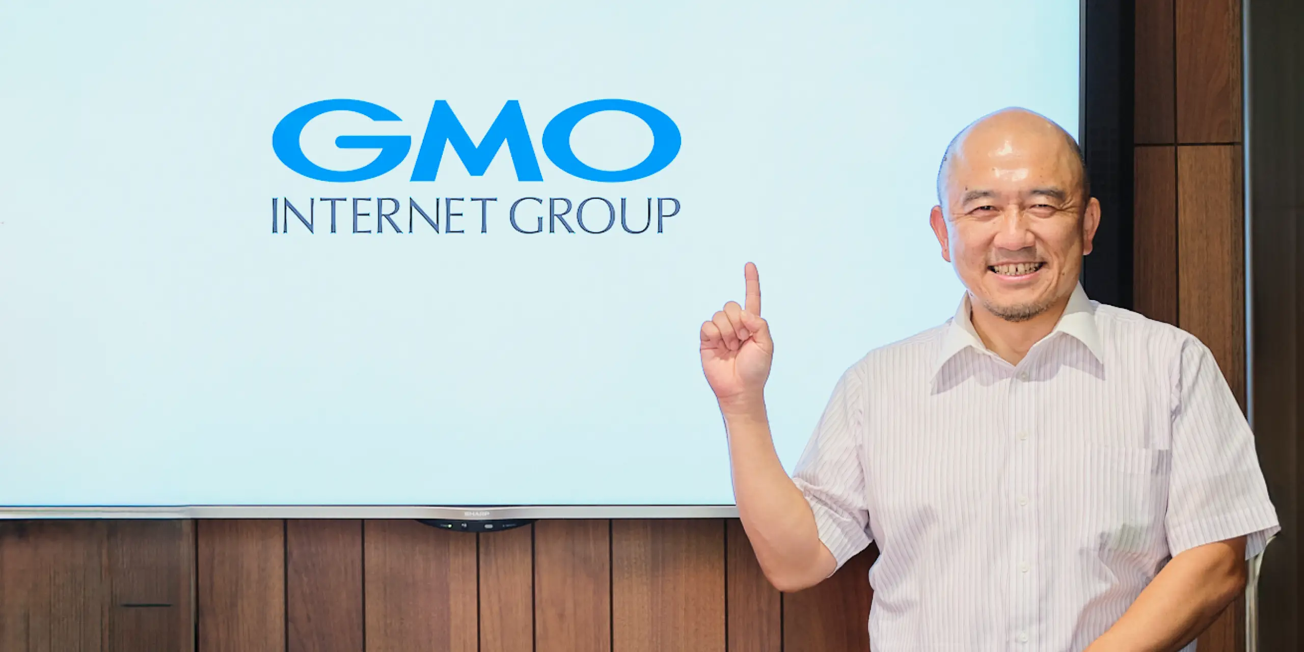 GMOあおぞらネット銀行、GMO INTERNET GROUPのロゴを背景に立つ金子邦彦氏の写真