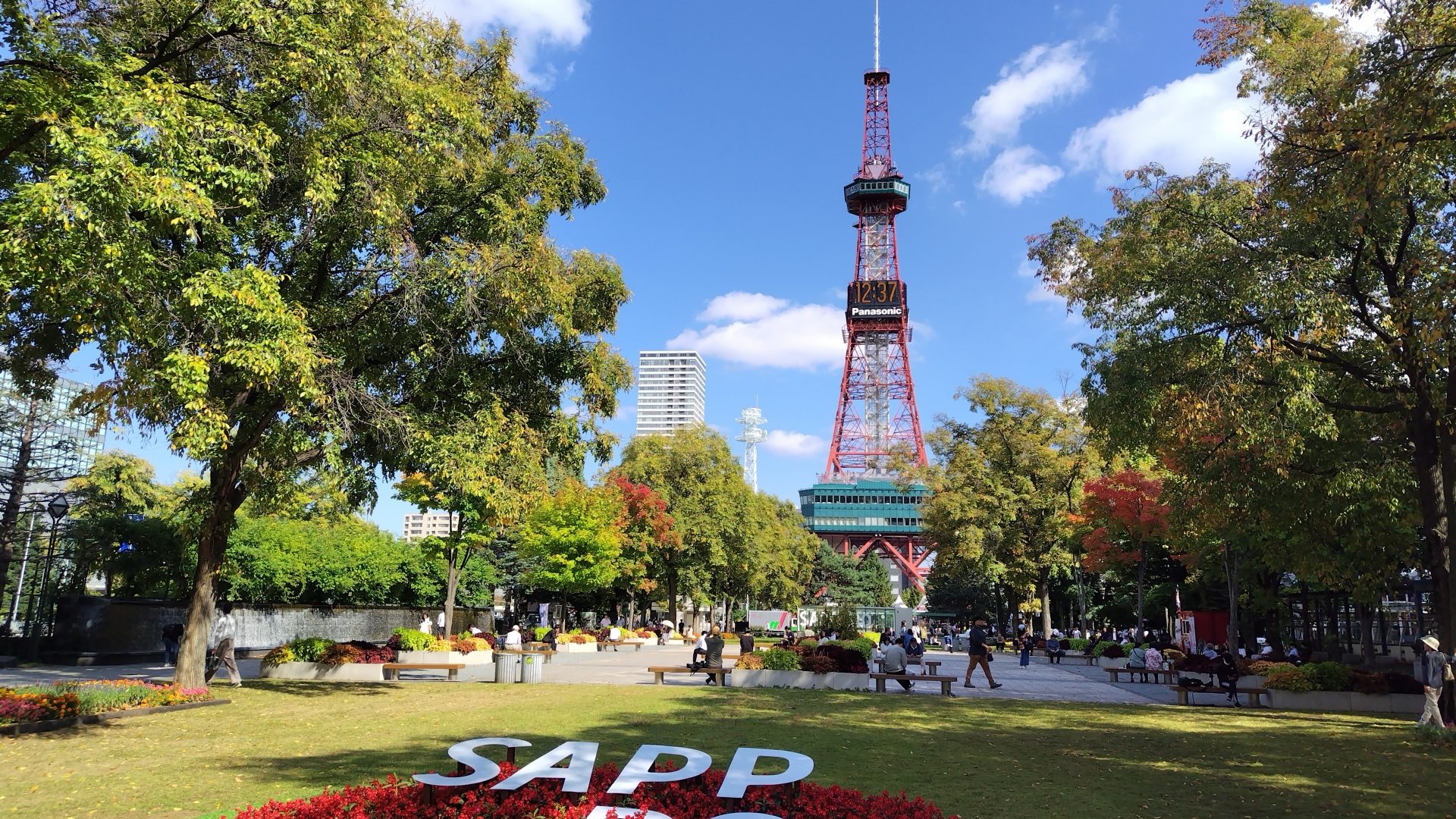 札幌 大通公園の写真です。青空とテレビ塔をバックに「SAPPORO」のモニュメントが映っています。